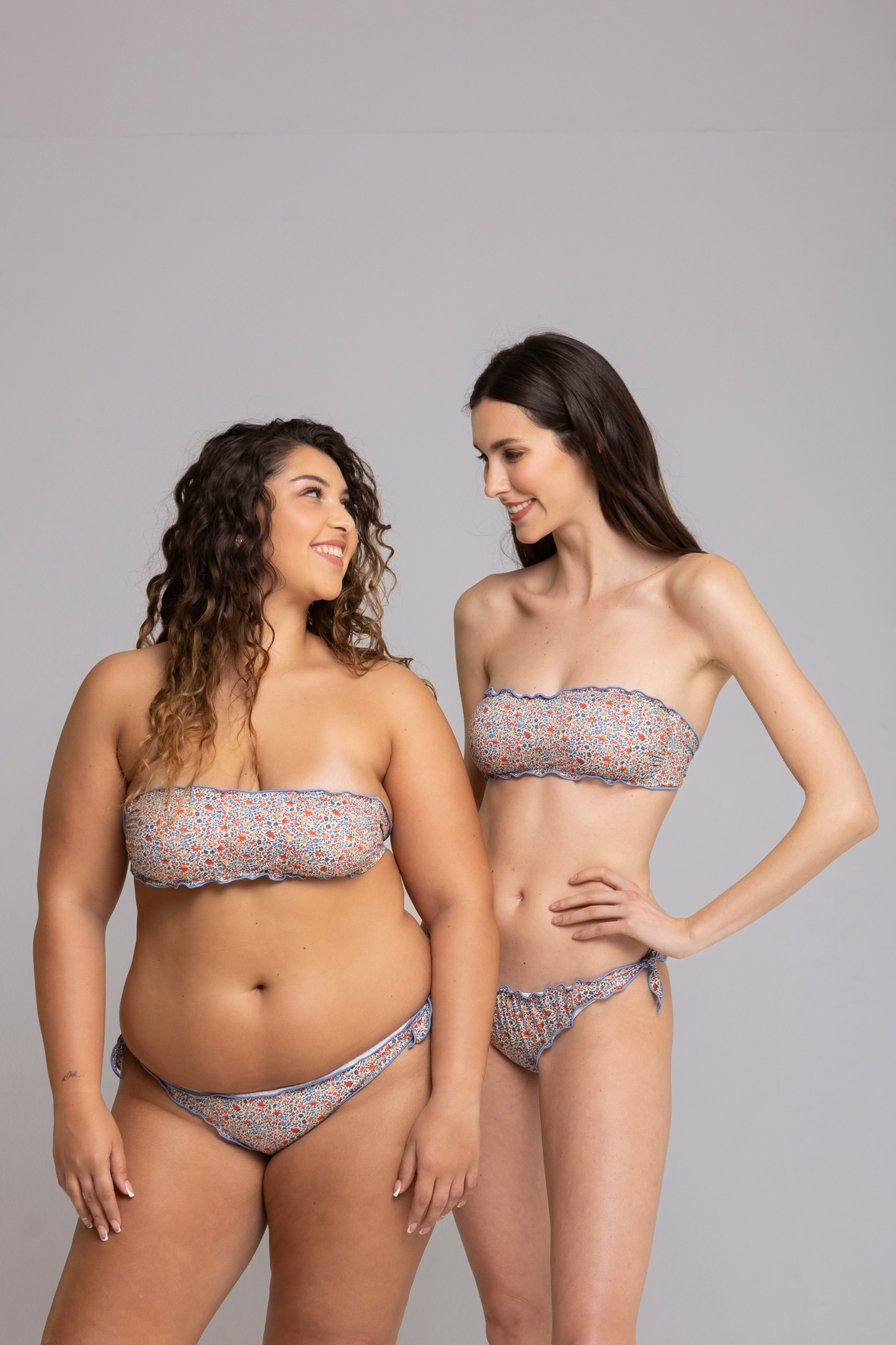 Two models wearing Fru Fru Blue Floral Fantasy Bandeau Bikini Set front view - one in size small, one in size large.