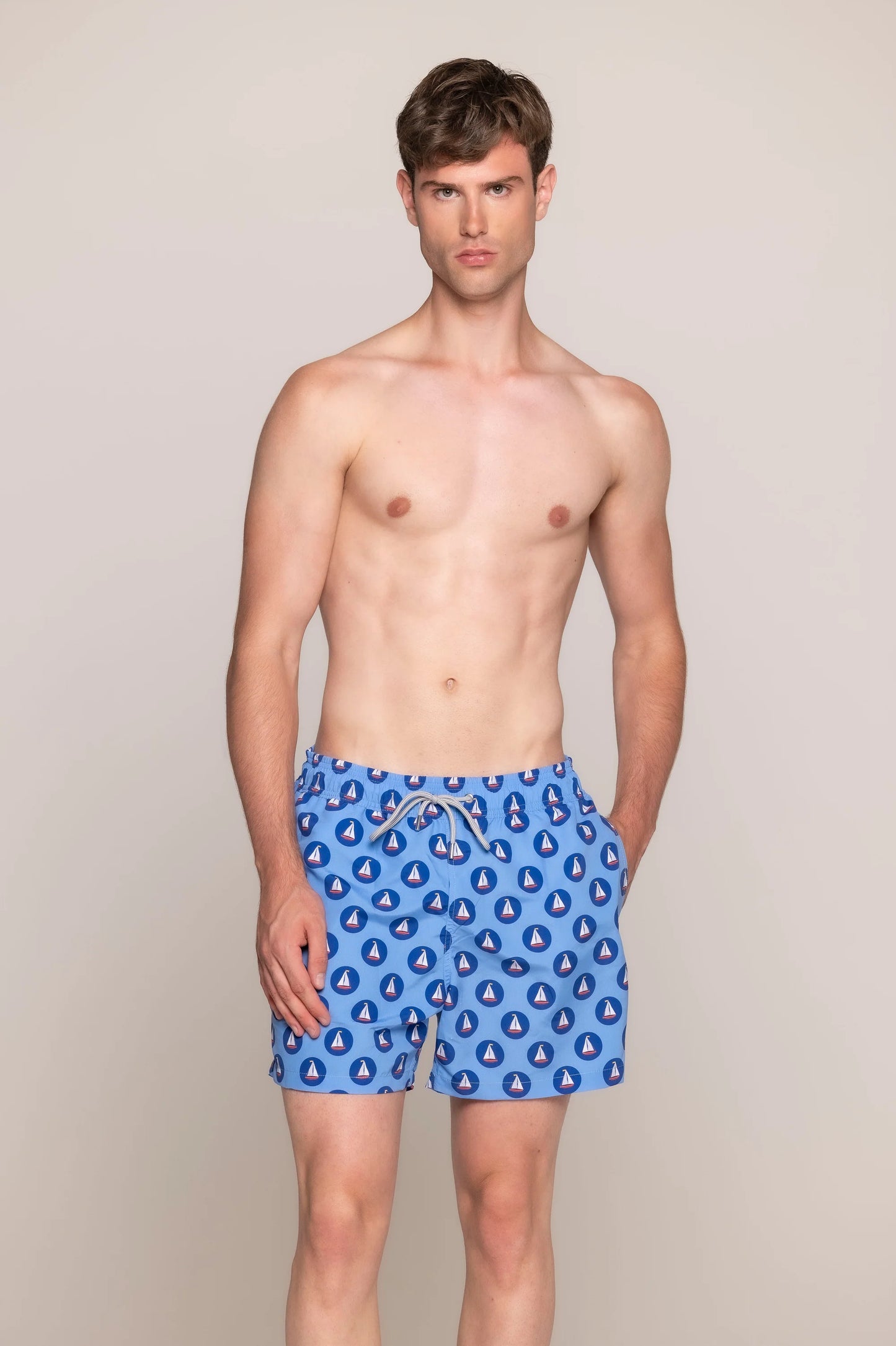 Men’s blue swim shorts with sailing boat print, featuring elastic waistband, side pockets, and back buttoned pocket - front view