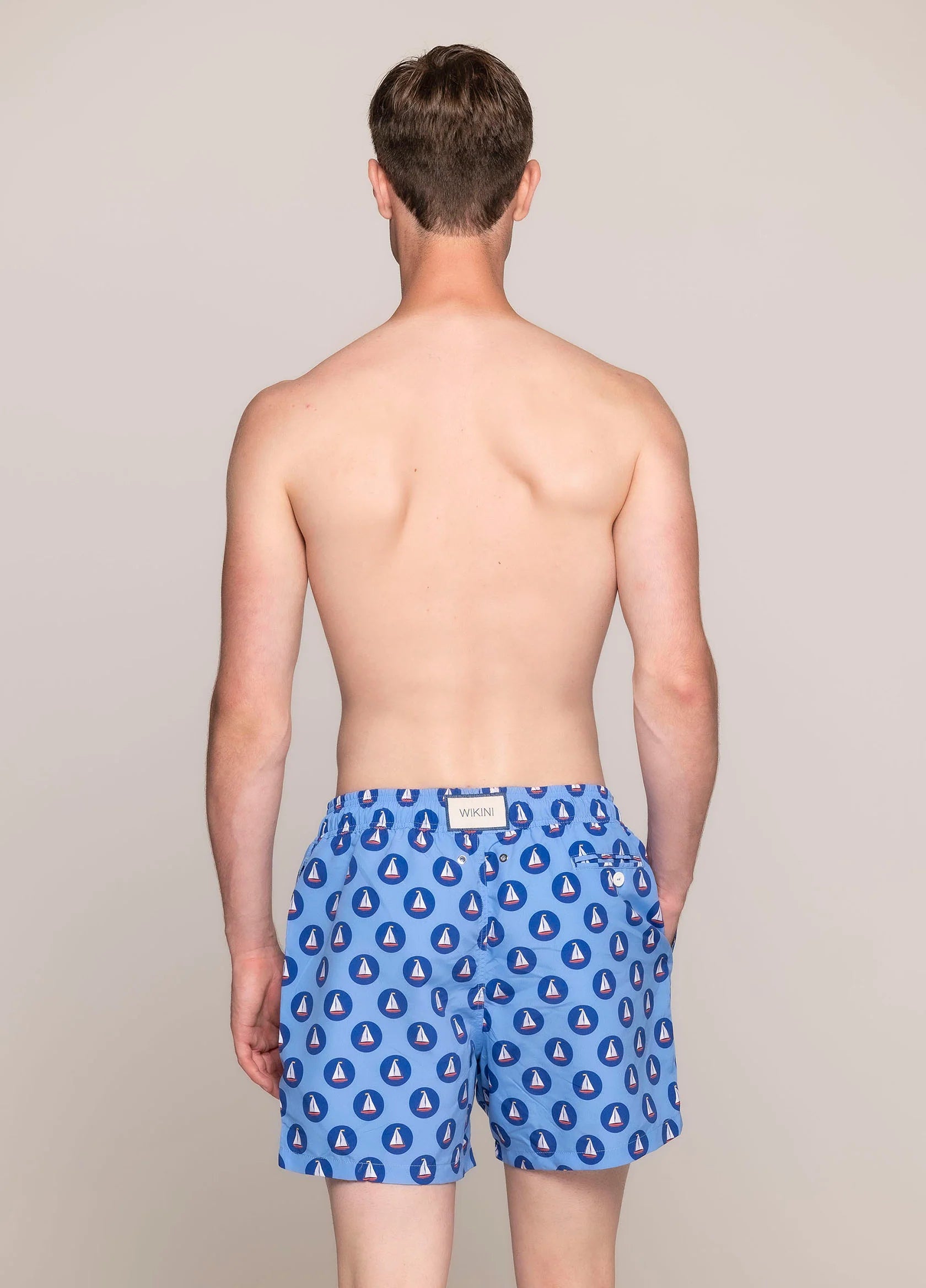 Men’s blue swim shorts with sailing boat print, featuring elastic waistband, side pockets, and back buttoned pocket - back view