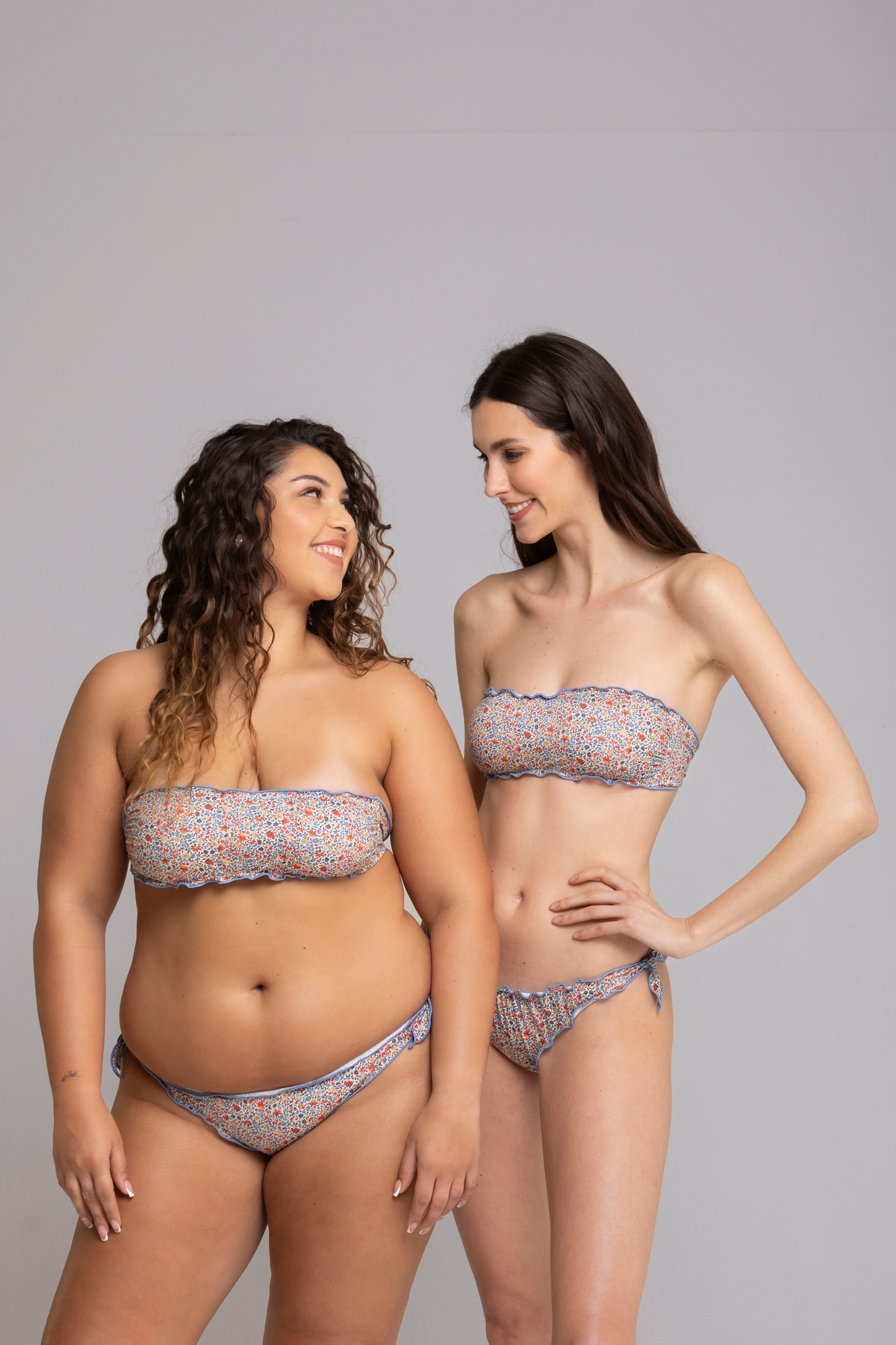 Two models wearing Fru Fru Blue Floral Fantasy Bandeau Bikini Set front view - one in size small, one in size large.