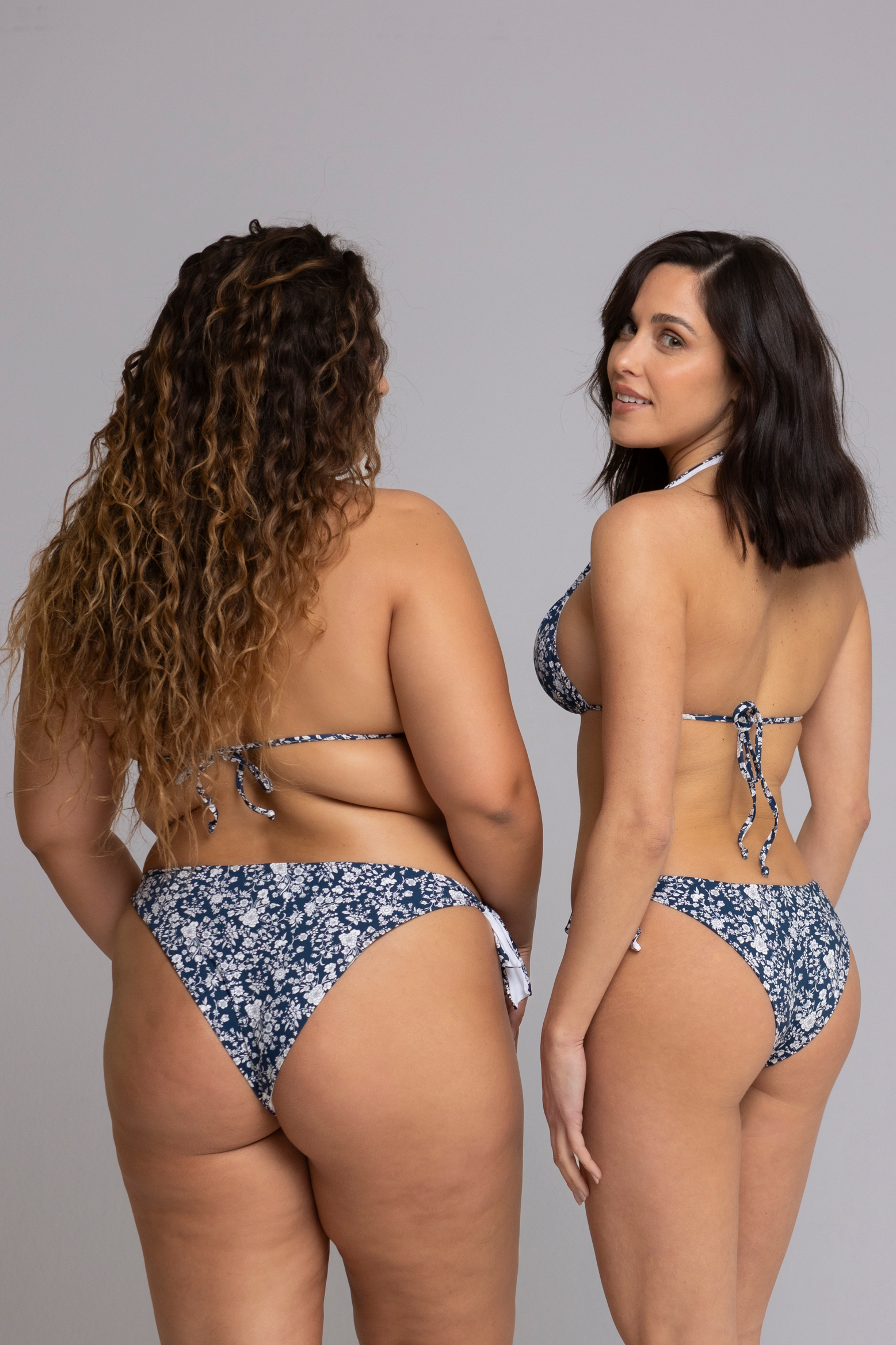 Two models wearing Floral Dark Blue and White Triangle Bikini Set back view — one in size small, one in size large.